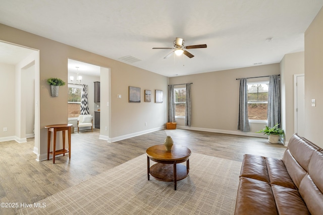 living room featuring ceiling fan with notable chandelier and light hardwood / wood-style flooring