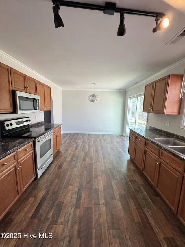 kitchen featuring dark wood-type flooring, rail lighting, hanging light fixtures, ornamental molding, and stainless steel appliances