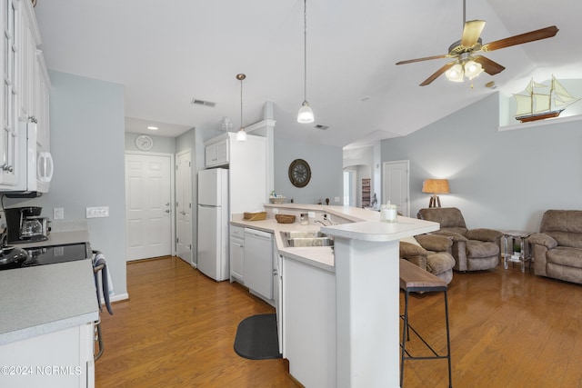 kitchen with white appliances, a breakfast bar, kitchen peninsula, and white cabinets