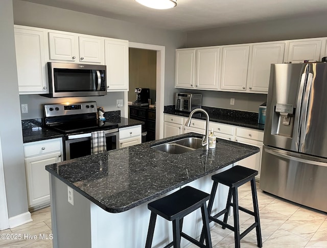 kitchen with stainless steel appliances, white cabinets, an island with sink, and sink