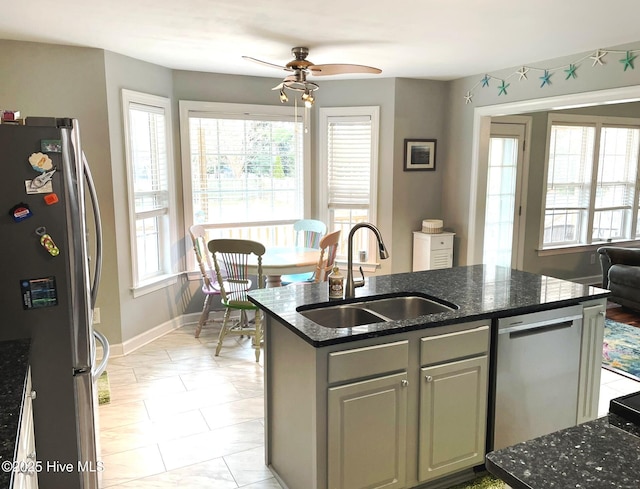 kitchen featuring stainless steel appliances, sink, ceiling fan, dark stone counters, and a kitchen island with sink