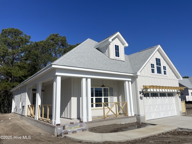 view of front of house with board and batten siding, covered porch, concrete driveway, and roof with shingles