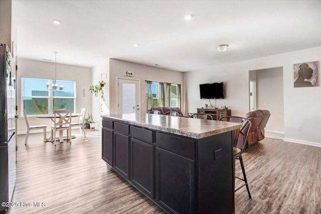 kitchen with wood-type flooring, hanging light fixtures, a kitchen island, a breakfast bar, and a notable chandelier