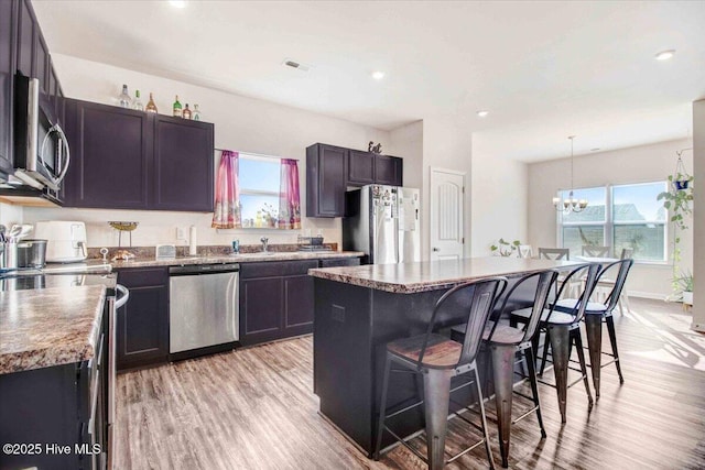 kitchen with light hardwood / wood-style flooring, a chandelier, a breakfast bar, a kitchen island, and appliances with stainless steel finishes