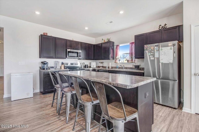 kitchen with stainless steel appliances, dark brown cabinetry, a kitchen bar, and a center island