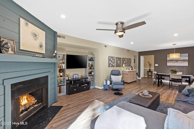 living room with wood-type flooring, ceiling fan, and built in shelves