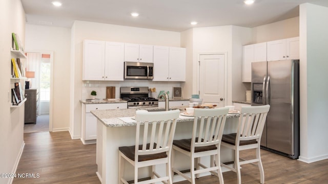 kitchen featuring light stone counters, an island with sink, appliances with stainless steel finishes, and white cabinetry