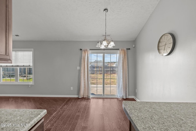 unfurnished dining area with an inviting chandelier, a textured ceiling, and dark hardwood / wood-style flooring