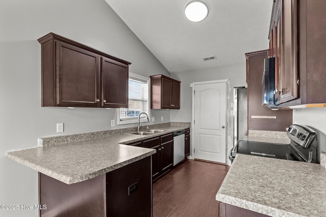 kitchen with vaulted ceiling, appliances with stainless steel finishes, sink, kitchen peninsula, and dark wood-type flooring