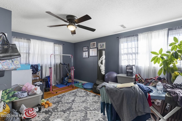 bedroom with ceiling fan, multiple windows, a textured ceiling, and hardwood / wood-style flooring