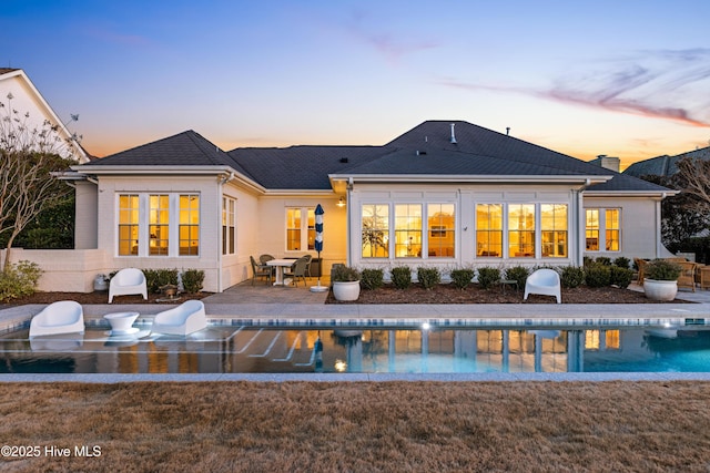 back house at dusk with a lawn and a patio