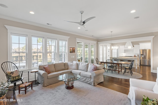 living room featuring ceiling fan with notable chandelier, wood-type flooring, plenty of natural light, and crown molding