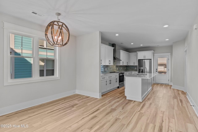 kitchen with white cabinets, stainless steel appliances, an island with sink, hanging light fixtures, and a notable chandelier