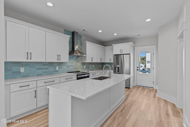 kitchen featuring white cabinetry, appliances with stainless steel finishes, a kitchen island with sink, wall chimney range hood, and sink