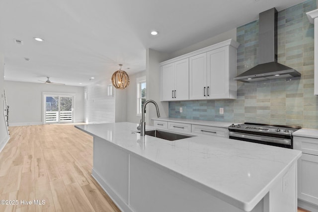 kitchen featuring wall chimney range hood, stainless steel electric range, sink, a kitchen island with sink, and white cabinets