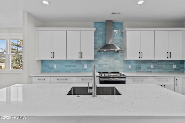 kitchen with wall chimney range hood, sink, white cabinetry, light stone countertops, and stainless steel range with electric cooktop