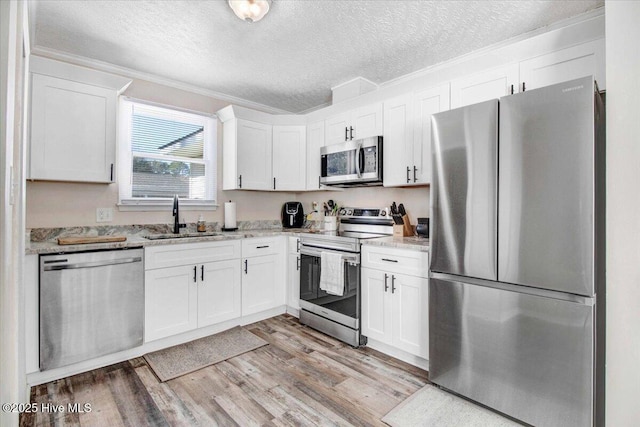 kitchen with light hardwood / wood-style floors, stainless steel appliances, light stone counters, sink, and white cabinetry