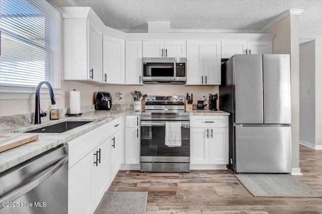 kitchen featuring stainless steel appliances, white cabinets, sink, and light stone countertops