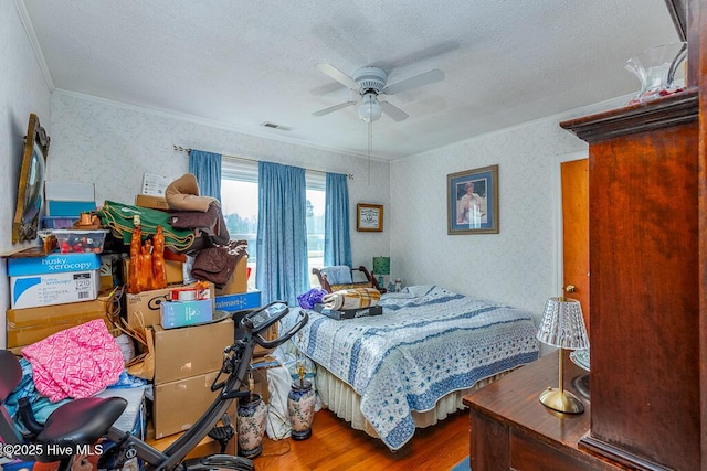 bedroom with wood finished floors, visible vents, wallpapered walls, a textured ceiling, and crown molding