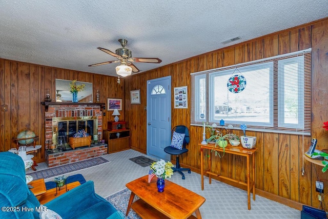 carpeted living room featuring a brick fireplace, wooden walls, a ceiling fan, and a textured ceiling