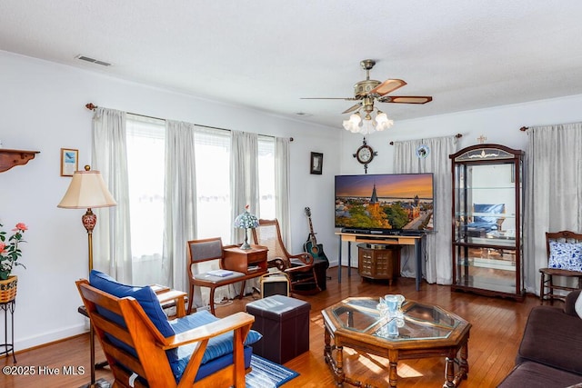 living room with baseboards, wood finished floors, visible vents, and ceiling fan