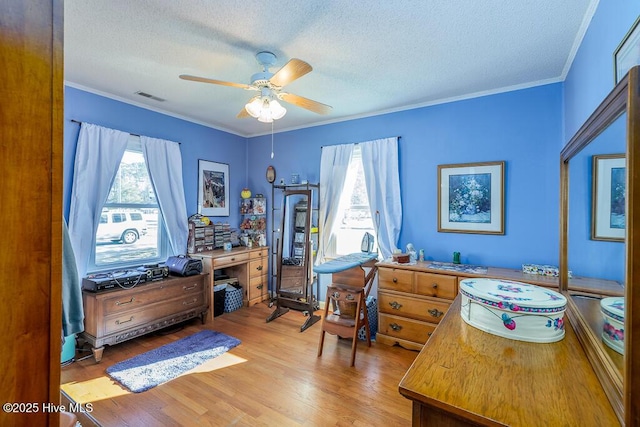 home office with visible vents, ceiling fan, ornamental molding, light wood-style floors, and a textured ceiling