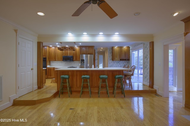 kitchen featuring tasteful backsplash, a center island, black appliances, a kitchen bar, and light hardwood / wood-style flooring