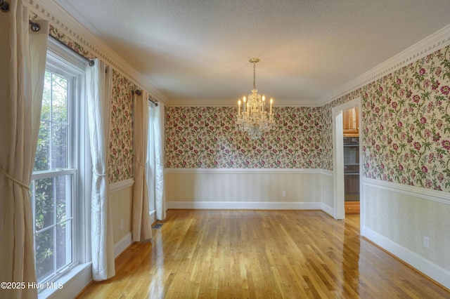 unfurnished dining area with a chandelier, light wood finished floors, wallpapered walls, and a wainscoted wall