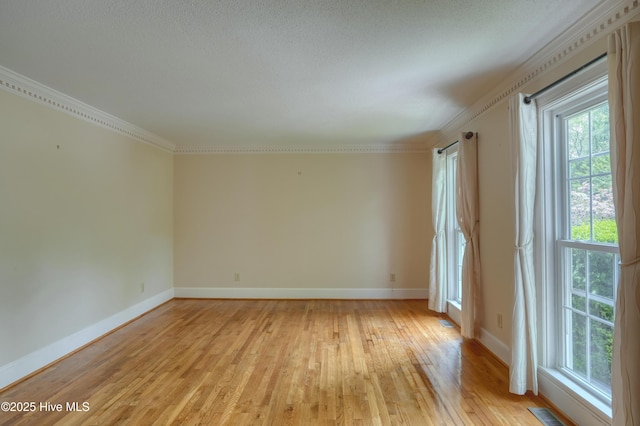 empty room featuring light wood-style flooring, crown molding, visible vents, and a wealth of natural light