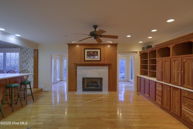 living room featuring light wood-type flooring, ceiling fan, crown molding, and a tiled fireplace