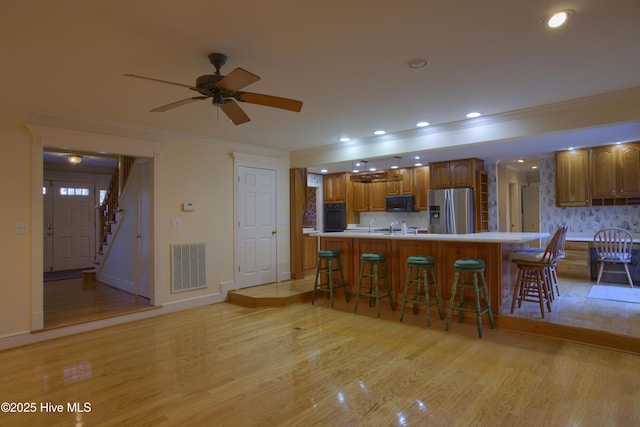 kitchen featuring light countertops, visible vents, brown cabinetry, a breakfast bar area, and black appliances