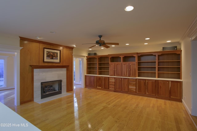 unfurnished living room featuring crown molding, ceiling fan, a tiled fireplace, and light wood-style floors