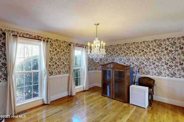 dining room featuring a textured ceiling, a chandelier, ornamental molding, and light hardwood / wood-style flooring