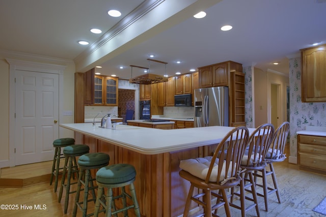 kitchen featuring light wood finished floors, a large island with sink, black appliances, and ornamental molding