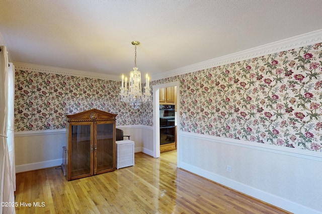 unfurnished dining area featuring an inviting chandelier, ornamental molding, and light hardwood / wood-style floors