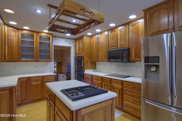 kitchen with glass insert cabinets, black appliances, light countertops, light wood finished floors, and backsplash