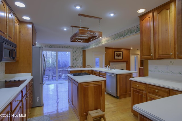 kitchen featuring kitchen peninsula, appliances with stainless steel finishes, a center island, light wood-type flooring, and sink