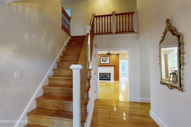 stairs with ceiling fan, a towering ceiling, and wood-type flooring