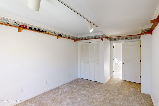 unfurnished bedroom with light colored carpet, a closet, ornamental molding, and rail lighting