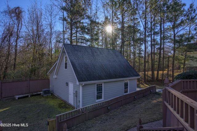 view of property exterior featuring central AC unit, fence, and roof with shingles