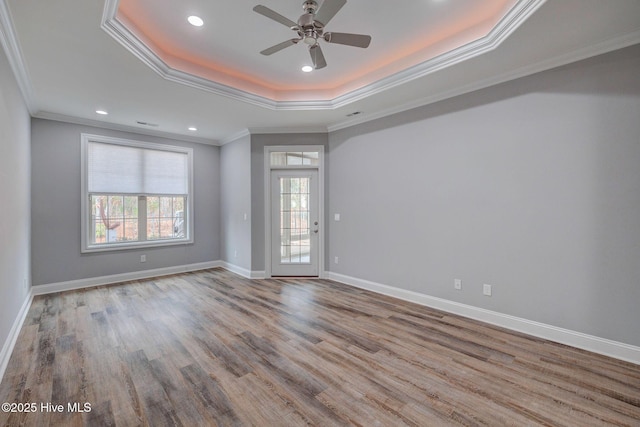 empty room with light wood-type flooring, ceiling fan, crown molding, and a raised ceiling