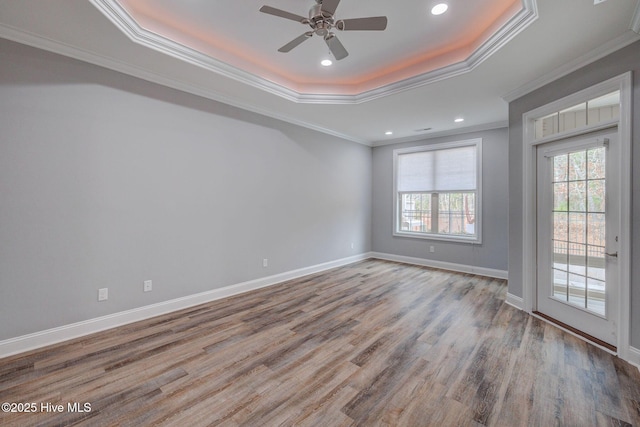 unfurnished room with ceiling fan, a raised ceiling, ornamental molding, and light wood-type flooring