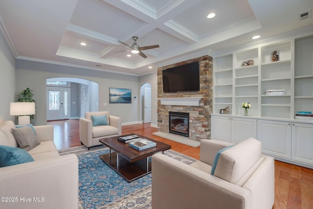 living room with light hardwood / wood-style floors, coffered ceiling, a fireplace, ornamental molding, and beamed ceiling