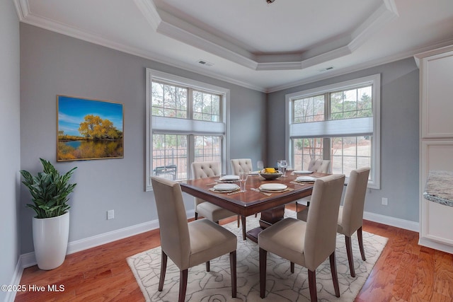 dining space featuring a tray ceiling, crown molding, and light wood-type flooring