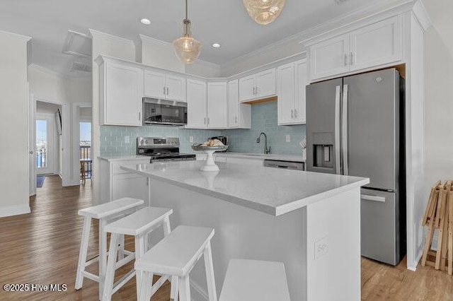 kitchen featuring appliances with stainless steel finishes, a center island, white cabinets, and decorative light fixtures