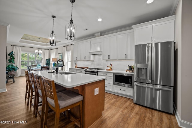 kitchen featuring stainless steel appliances, an island with sink, custom range hood, white cabinets, and sink