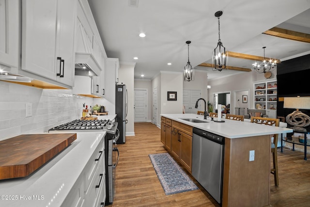 kitchen with stainless steel appliances, a center island with sink, white cabinetry, and hanging light fixtures