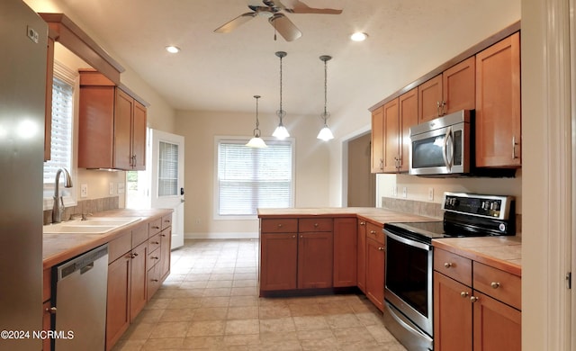 kitchen with tile counters, appliances with stainless steel finishes, a healthy amount of sunlight, sink, and decorative light fixtures