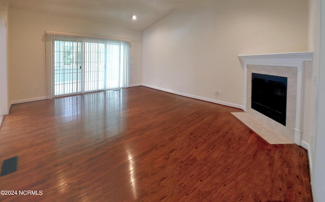 unfurnished living room featuring a tiled fireplace, dark hardwood / wood-style flooring, and vaulted ceiling