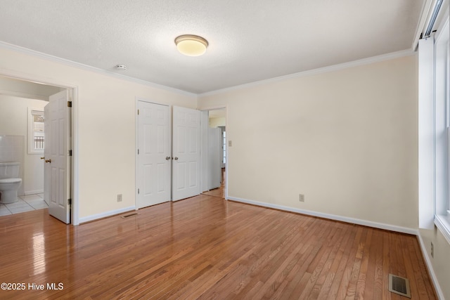 unfurnished bedroom featuring ensuite bathroom, a closet, crown molding, and light hardwood / wood-style flooring